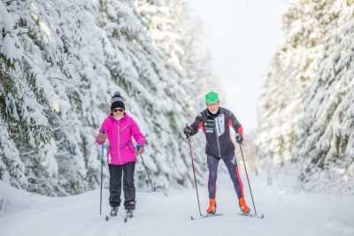 nainen ja mies hiihtävät lumisessa metsässä