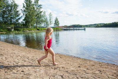 tyttö juoksee hiekkarannalla uimaan järveen