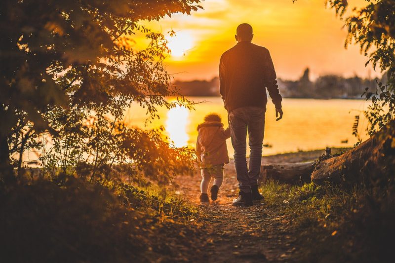 isä ja lapsi kulkevat järven rannalla ilta-auringossa